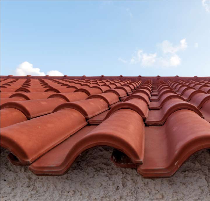Low-angle detail shot of perfectly aligned red clay roofing tiles showcasing the waterproof interlocking design used in high-end tile roof repairs.