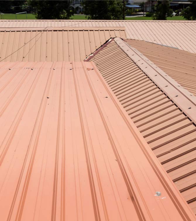 Terracotta-colored corrugated metal roof panels installed on a residential property, featuring multiple roof planes and flashed valleys for effective water runoff.