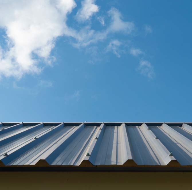 Durable silver galvanized steel roof sheets secured with neoprene-washer fasteners, showcasing a clean and rust-free industrial roofing system under a blue sky, after iron roof repairs.