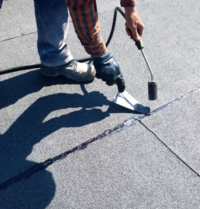 Professional roofing technician in the Bay Area using a propane torch to heat-weld seams for flat roof repairs  on a durable modified bitumen torch-down flat roof system.
