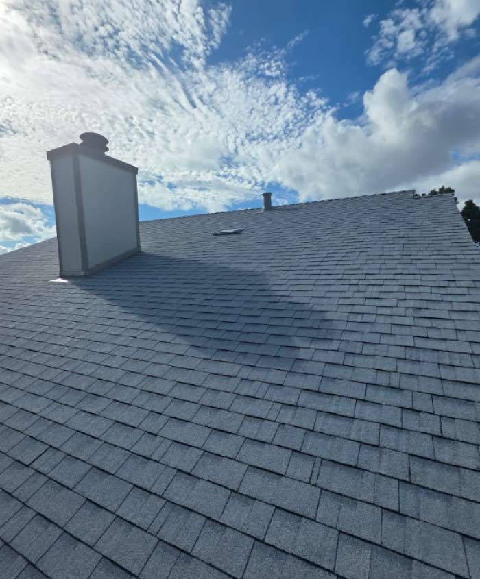 Reddish-brown asphalt shingle roof installed on a yellow brick home featuring complex valleys and a brick chimney.