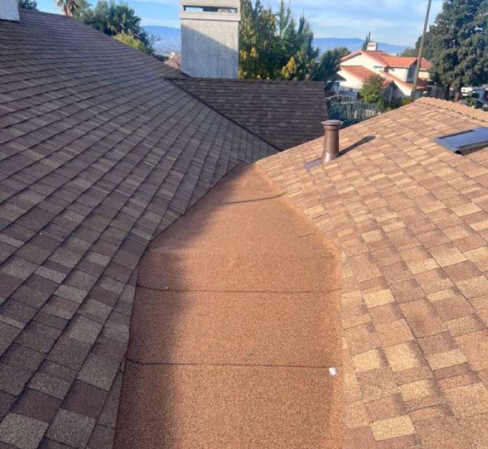 Close-up view of a newly installed dark brown architectural asphalt shingle roof section intersecting with a light-colored stucco exterior wall.