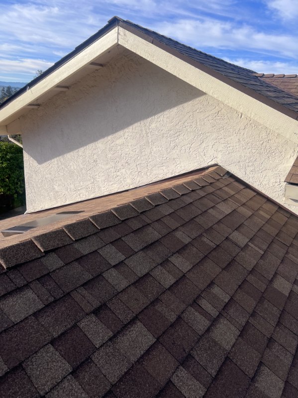 Close-up detail of a brown stamped metal roof tile system with a matching seamless brown gutter and downspout connection.