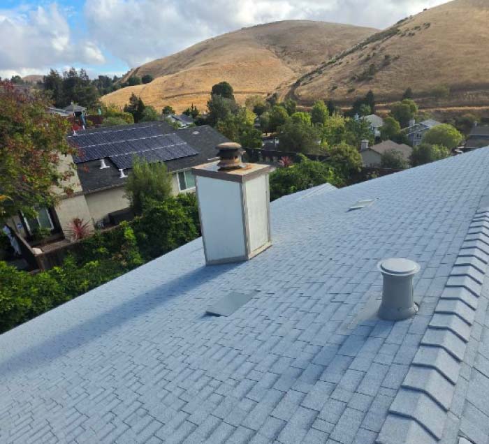 Wide shot of a completed residential roofing project on a sunny day, highlighting a straight ridge cap and integrated plumbing vent boots.
